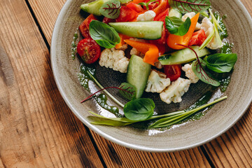 There is a gray plate of the vegetarian food on the wooden table.