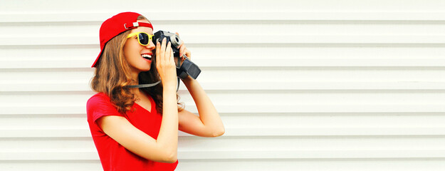 Portrait of happy smiling young woman photographer taking picture on film camera wearing red baseball cap on white background, blank copy space for advertising text - Powered by Adobe