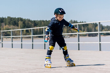 A child rides blue yellow and white roller skates. Little boy in protective gear learning to...