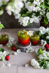 Strawberry matcha latte in transparent glasses on a table with flowers. Preparation of refreshing cold drinks. Healthy food. Raw cuisine of fruits, berries and green tea.