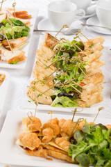 Festive Buffet. An assortment of cold snacks on wooden skewers. Decorated with lettuce leaves and served on rectangular plates against the background of saucer cups