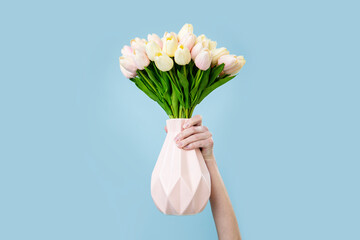 A woman's hand holds a vase with a bouquet of tulips on a blue background