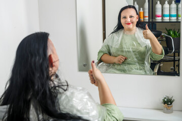 A smiling woman with a half-shaved head in a barber's chair shows a class reflection in the mirror.