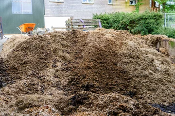 Deurstickers Wheelbarrow beside a large pile of horse manure and bedding © Stephen