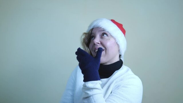 Cheerful forty-year-old woman in a red New Year's hat and a white sweater. Woman in winter gloves. Merry Cristmas