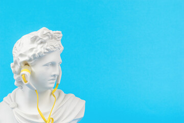 The figure of Apollo with yellow headphones on a blue background. Minimal concept.
