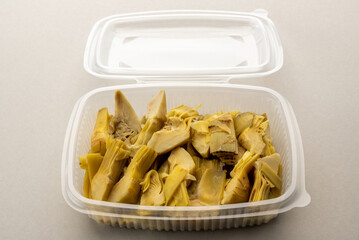 Boiled artichokes wedges in transparent food-grade plastic box for refrigeration or storing, on...