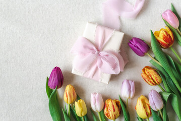 Flat lay of a beautifully wrapped gift decorated with a silk ribbon and surrounded by spring tulips.