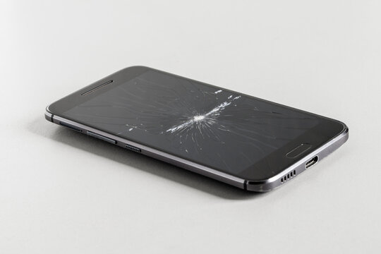 Smartphone with a broken screen on a white table. Broken display, cracked glass
