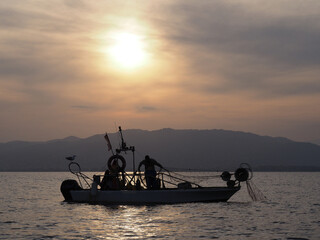 pêcheur remontant un filet sur son bateau au coucher du soleil - Méditerranée