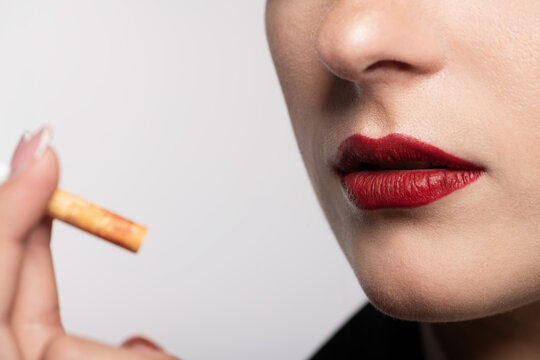 Close-up portrait of woman lips with red lipstick holding cigarette in her hands near face. Selective focus and image with shallow depth of field. White studio background with copy space