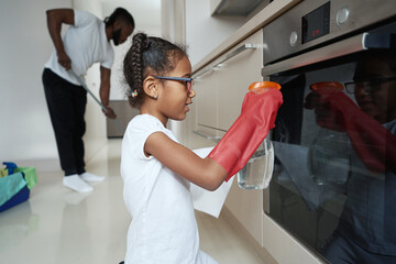 Little african american girl washing oven door next to father