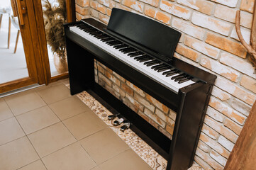A modern expensive black piano, a musical instrument stands against the backdrop of a brick wall in...