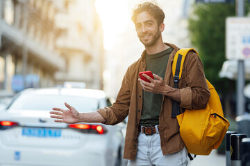 Outdoor portrait of handsome young hipster man with mobile phone waiting for taxi. - obrazy, fototapety, plakaty