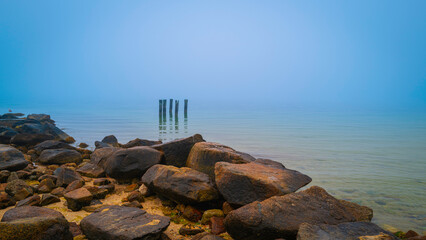 Seascape on Cape Cod on a foggy morning over the glacial rocks of jetty and five pillars of the...