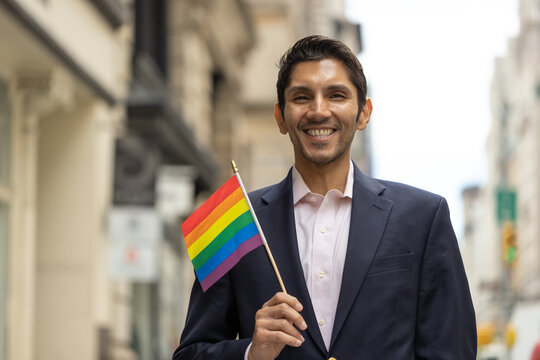LGBTQ gay man holding a rainbow flag on city street portrait smiling happy