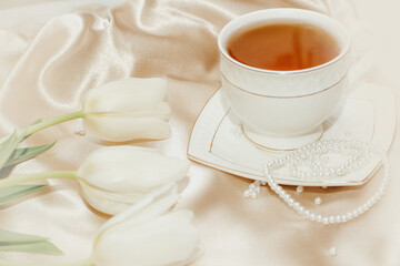 Bouquet of white tulips with pearl beads and tea on silk golden nude satin background.