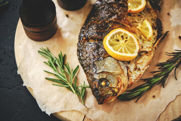 Baked fish in oven with lemon and rosemary laid out cutting board and parchment paper.On dark...