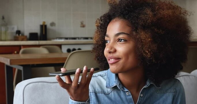 Smiling African lady hold modern cellphone close to mouth speak text to translate online via ai app say request to find information at web. Happy young woman record voicemail enjoy easy communication