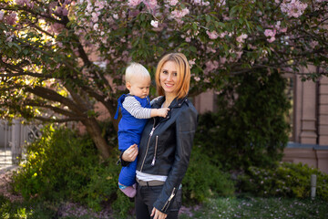Fototapeta premium mother and little boy son having fun in spring park near pink sakura blooming tree. Spring concept