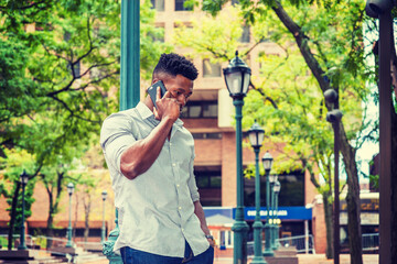 African American Man calling outside, wearing gray shirt, rolling over sleeves, standing against light pole on street in New York, lowering head, listening to cell phone.  filtered effect..
