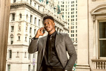 African American Businessman working in New York. Wearing fashionable jacket, black undershirt, necktie, young guy with little goatee, standing by vintage style office building, calling on cell phone