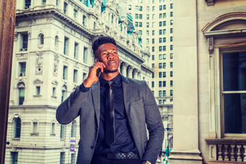 African American Businessman working in New York. Wearing fashionable jacket, black undershirt, necktie, young guy with little goatee, standing by vintage style office building, calling on cell phone