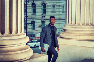 African American Businessman traveling, working in New York, wearing fashionable jacket, necktie, carrying laptop computer, walking into vintage office building from street. iltered effect..