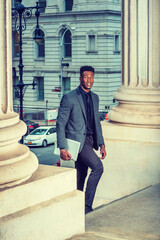 African American Businessman traveling, working in New York, wearing fashionable jacket, necktie, carrying laptop computer, walking into vintage office building from street. filtered effect..