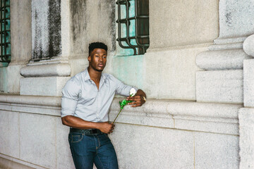 African American Man seeking love in New York, wearing gray shirt, blue jeans, wristwatch, standing by wall on street, holding white rose, waiting for you. I missing You. filtered effect..