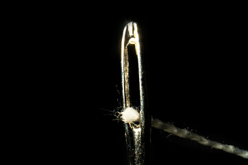 Macro image of a needle eye threaded with piece of white thread on black background. Steel shiny tailor's needle with permeation thread close up. The tool for sewing, embroidery, repair of clothes.