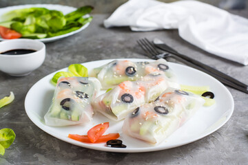 Fresh spring rolls in rice paper made from shrimp, olives and vegetables on a plate on the table.