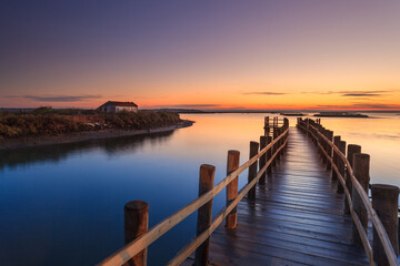 Fototapeta na wymiar Amazing romantic view from the pier at sunset. Serene landscape on the lake at colorful sunset. Old wooden pier in a fineart photo