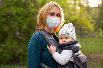 Young woman in medical mask with a child in her arms happy, blossom in spring Park, covid concept