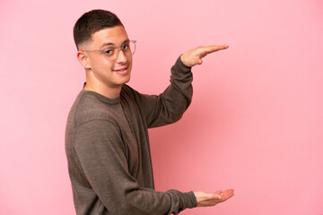 Young Brazilian man isolated on pink background holding copyspace to insert an ad