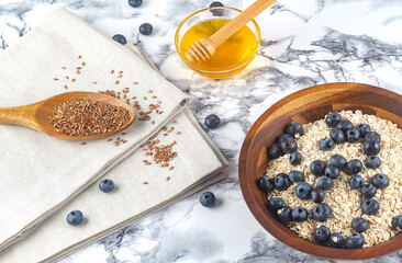 Fototapeta premium Oatmeal with blueberries on a wooden plate with honey and flax seed on wooden spoon, background for breakfast in the morning