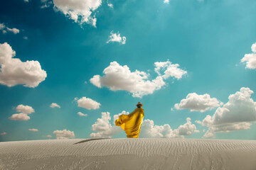 Woman in hat and arabic yellow clothes on dune in desert.