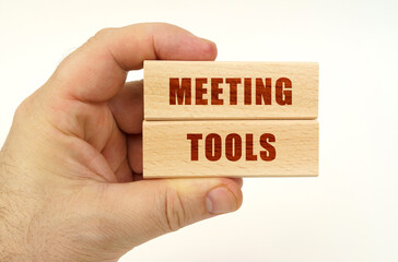 On a white background, a hand that holds wooden blocks with the inscription - Meeting Tools