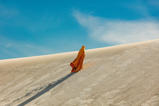 woman in yellow arabic clothing climbing a dune in the desert