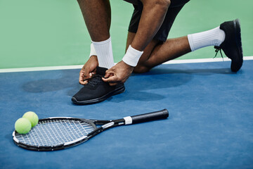 Close up of unrecognizable black sportsman tying shoelaces at tennis court, copy space