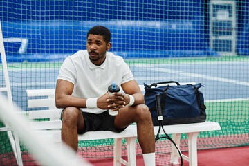 Portrait of black professional sportsman drinking water while taking break in tennis court, copy...