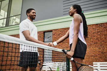 Side view shot of two smiling tennis players shaking hands across net during match at court