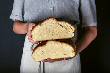 Female hands holding freshly baked sourdough artisan bread sliced in halfs. Homemade with wheat flour and starter. Dark rustic style.  