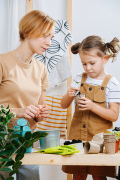 Mother looking over her daughter planting a seedling in a paper case
