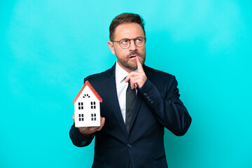 Real estate middle age agent man isolated on blue background having doubts while looking up