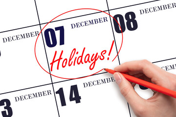 Hand drawing a red circle and writing the text Holidays on the calendar date 7 December. Important date.