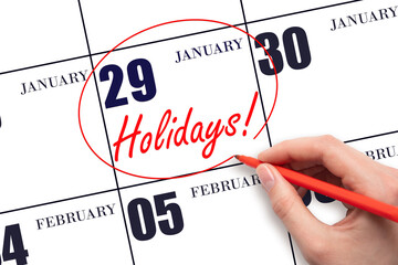 Hand drawing a red circle and writing the text Holidays on the calendar date 29 January. Important date.