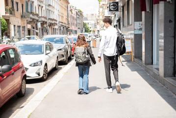 due giovani che camminano di spalle per strada con zaino della scuola