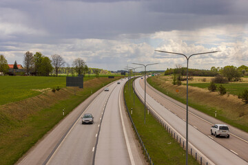 Beautiful top view of E4 highway with several cars. Green side fields and stormy sky background. Sweden.
