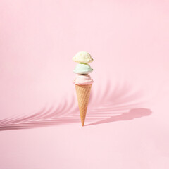 Ice cream with three scoops in a cone placed vertically along with palm leaf shade on pink background. Minimal summer concept.